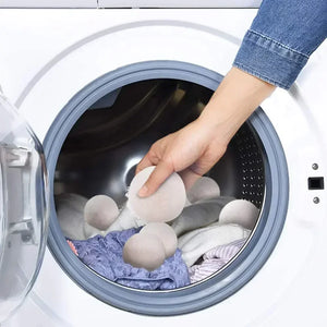 Una mano mette le palline per asciugatrice bianco naturale nel cestello insieme al bucato