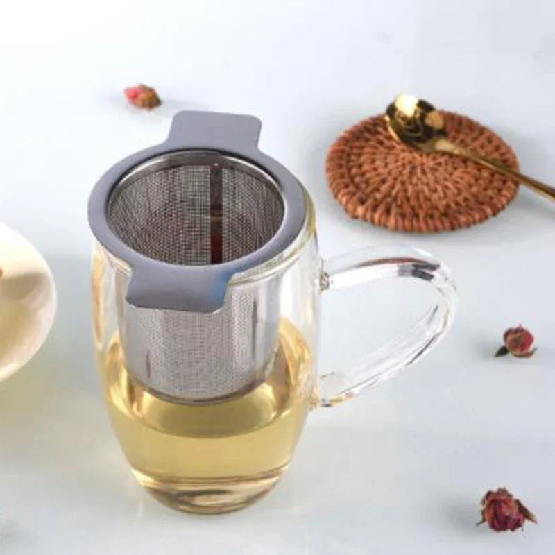 Filtro per tè in acciaio inox con due manici su una tazza di vetro