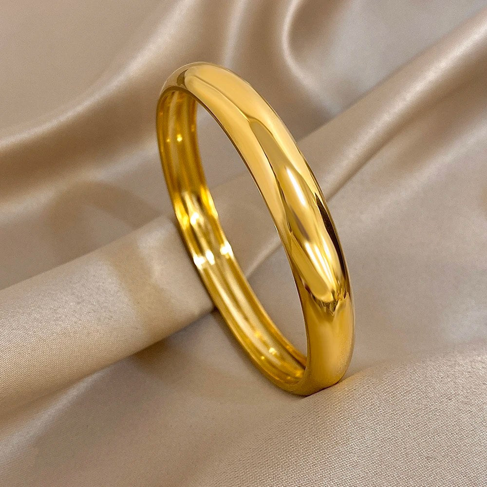 Bracciale rigido color oro in piedi su un raso beige
