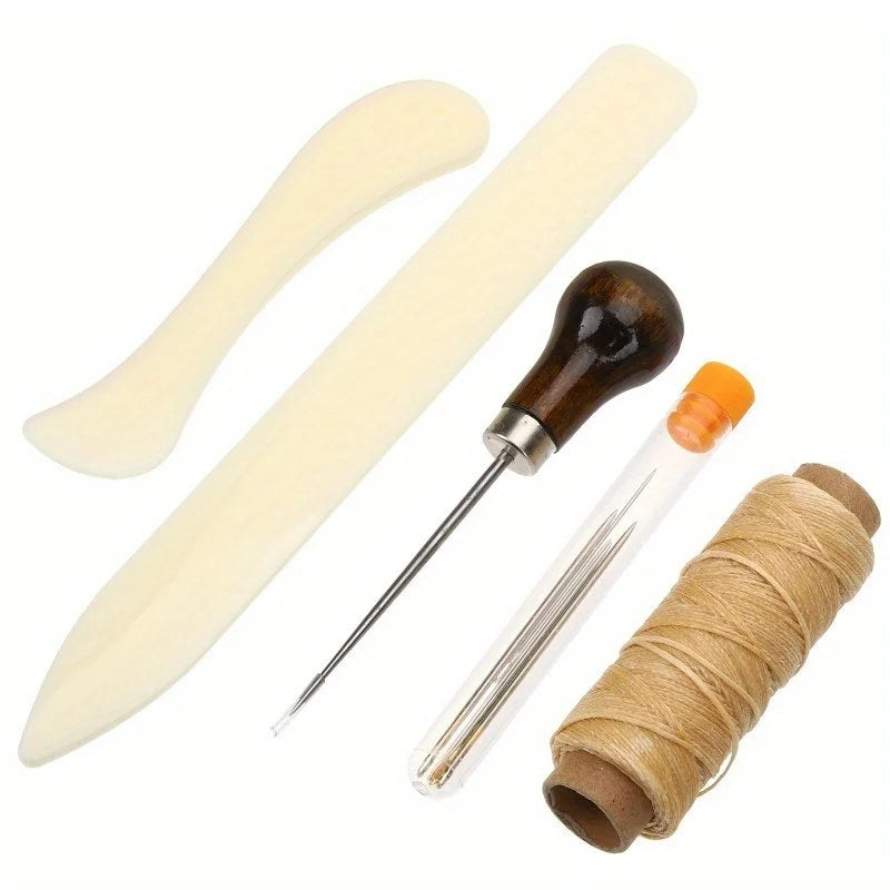 Kit rilegatura a mano su fondo bianco: stecca piegacarta lunga, stecca curva, punteruolo con manico in legno, aghi in un tubetto e filo cerato