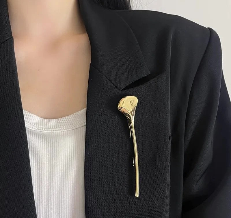 Spilla color oro a foglia di ginkgo appuntata in verticale su una giacca nera