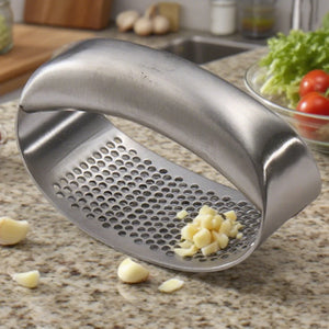 Spremiaglio curvo in acciaio inox con aglio schiacciato su un piano di lavoro della cucina