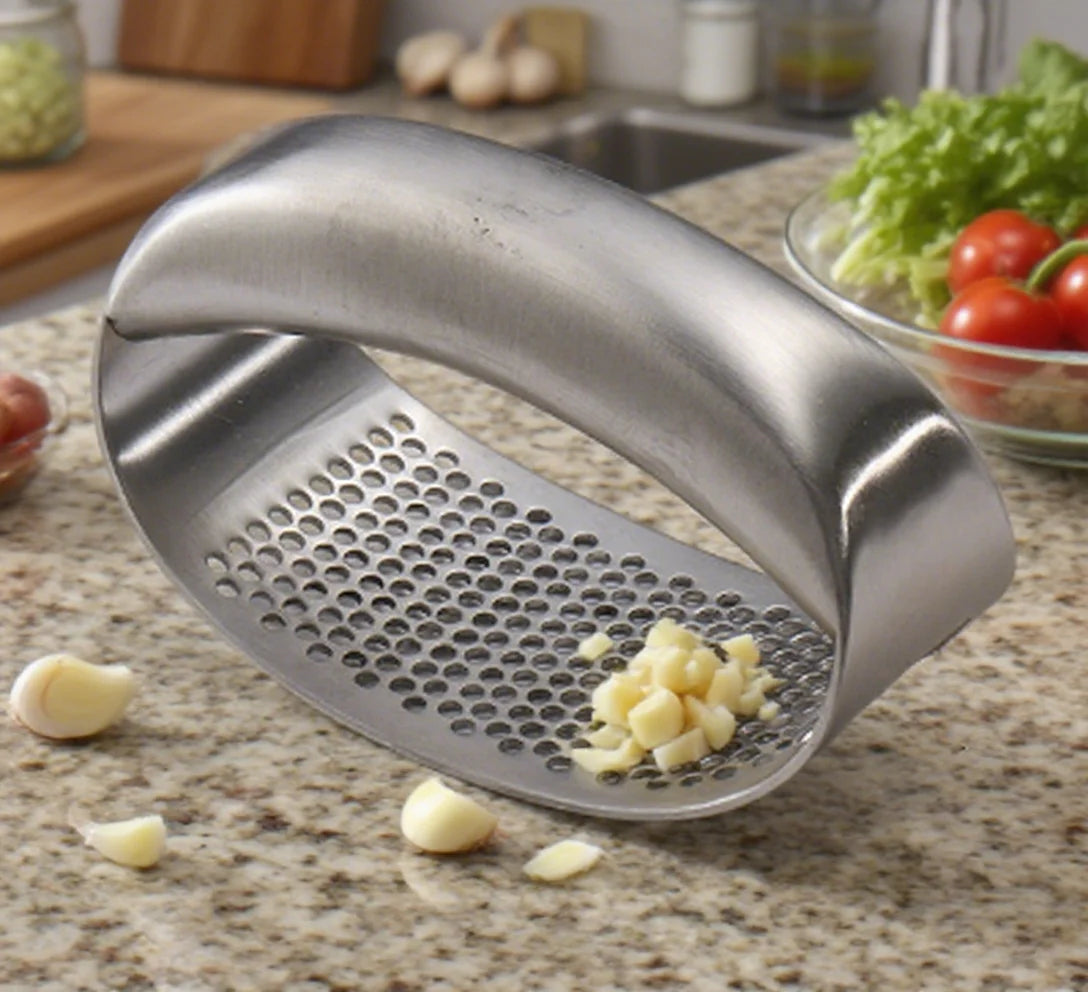 Spremiaglio curvo in acciaio inox con aglio schiacciato su un piano di lavoro della cucina
