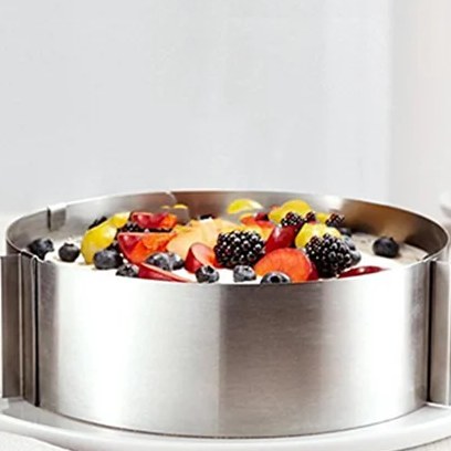 Anello per torte regolabile in acciaio inox intorno a una torta con frutti di bosco e frutta