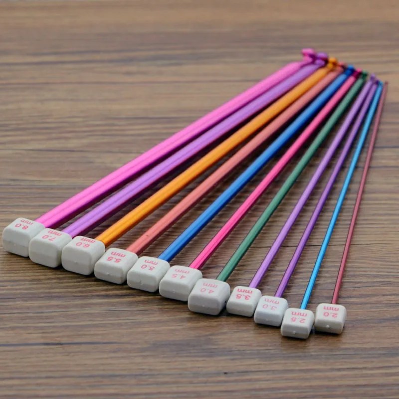 11 uncinetti tunisini colorati su un tavolo di legno, misure da 2,0 a 8,0 mm stampate sui fermi bianchi