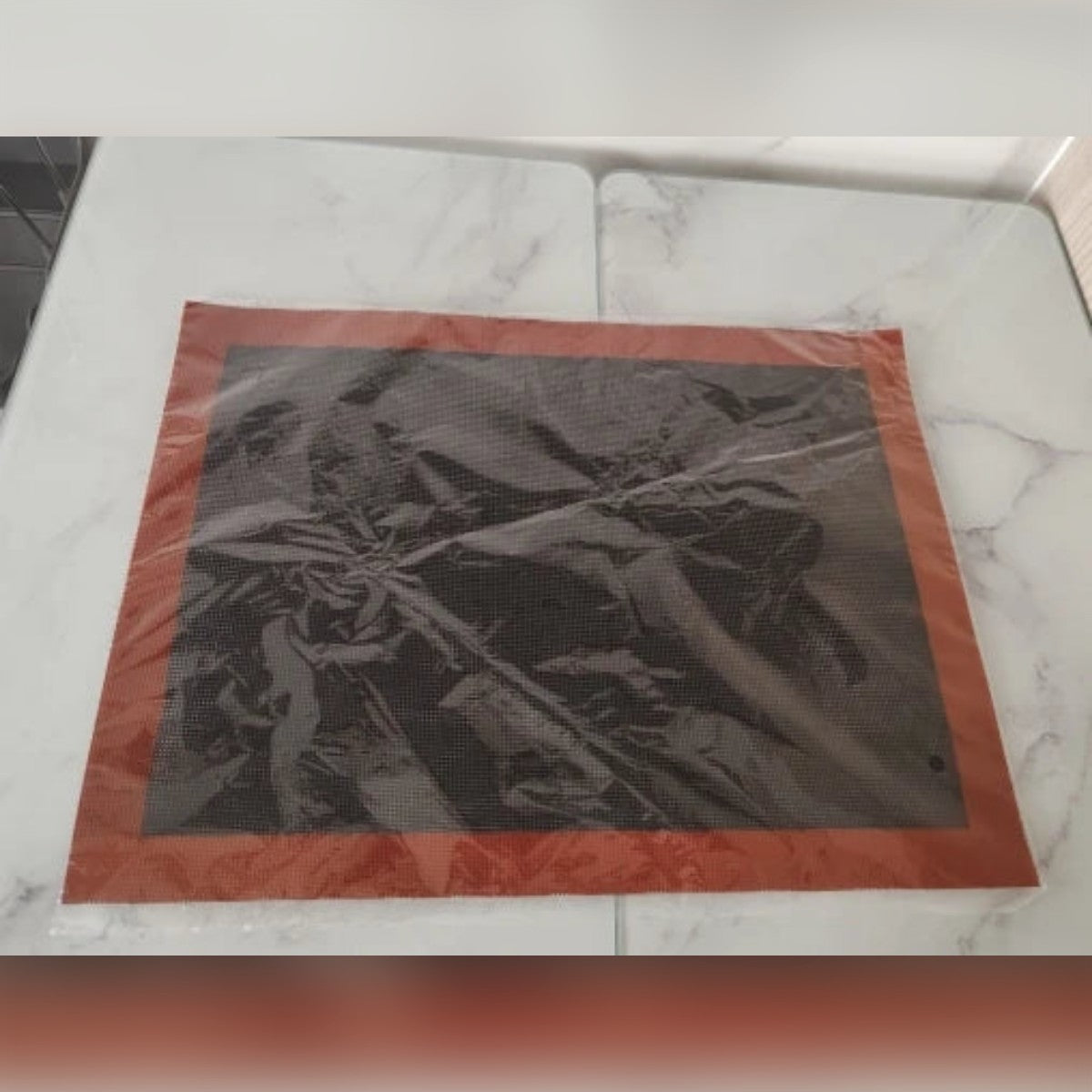 Foto di un acquirente: il tappetino forato nella sua busta trasparente su un tavolo di marmo