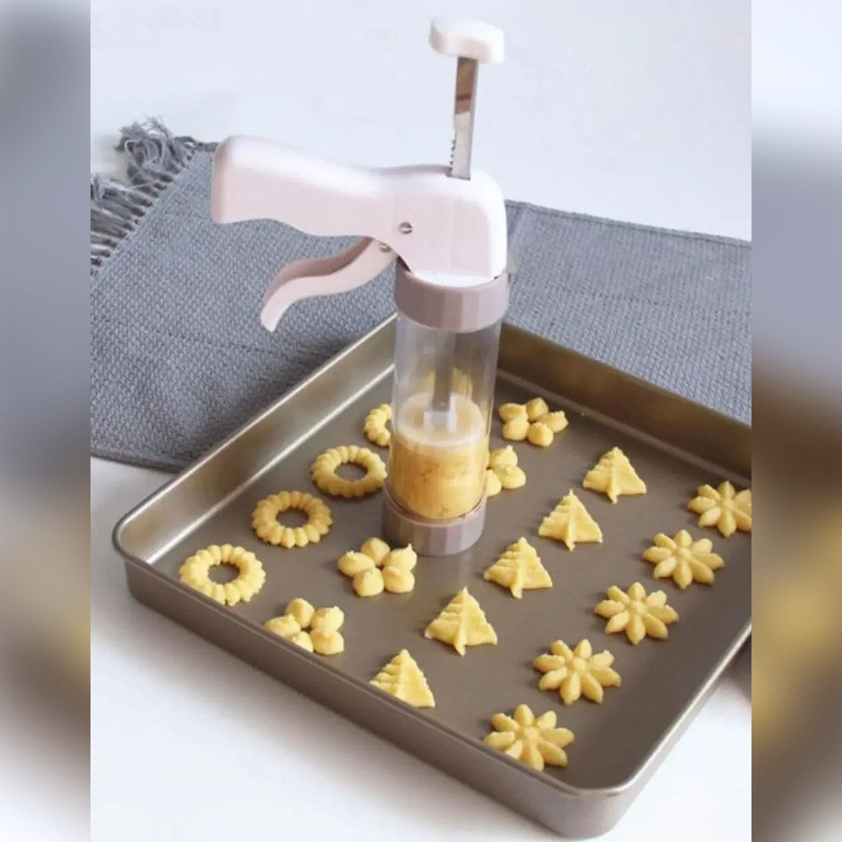La sparabiscotti in piedi su una teglia con biscotti a fiore, ad anello e ad alberello