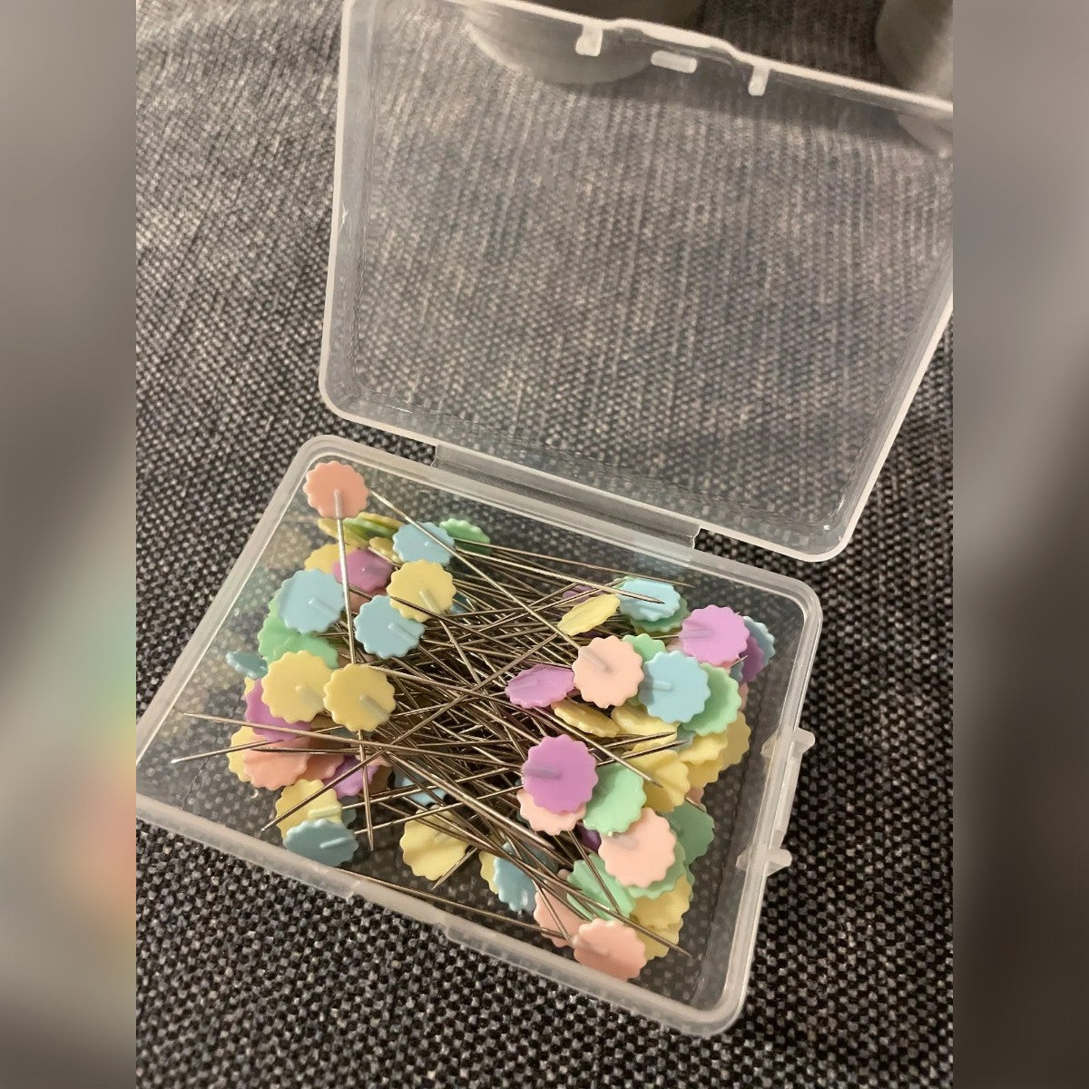 Foto di un acquirente: gli spilli nella scatola aperta su un tessuto grigio