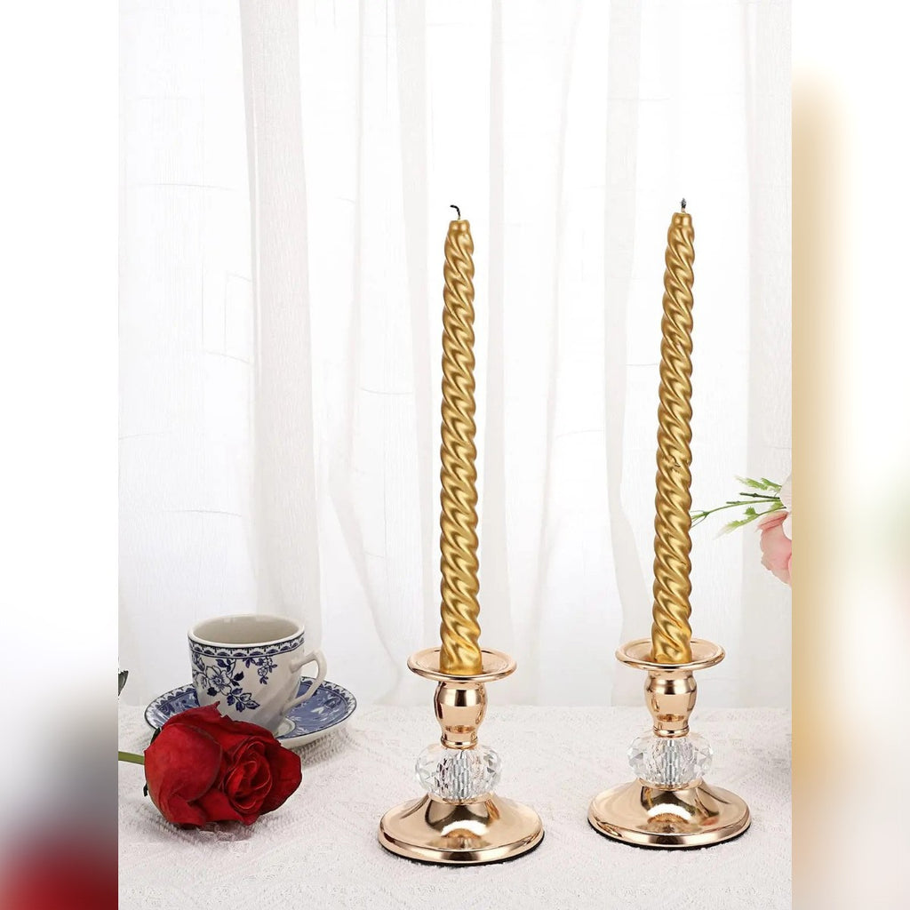 Due candelieri color oro con candele lunghe dorate davanti a una tenda bianca
