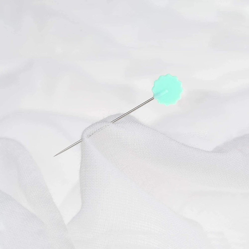 Uno spillo con la testa a fiore verde menta infilato in un tessuto bianco