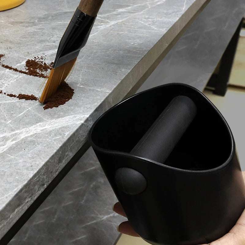 Il battifondi tenuto al bordo del bancone mentre i fondi di caffè vengono spazzati dentro