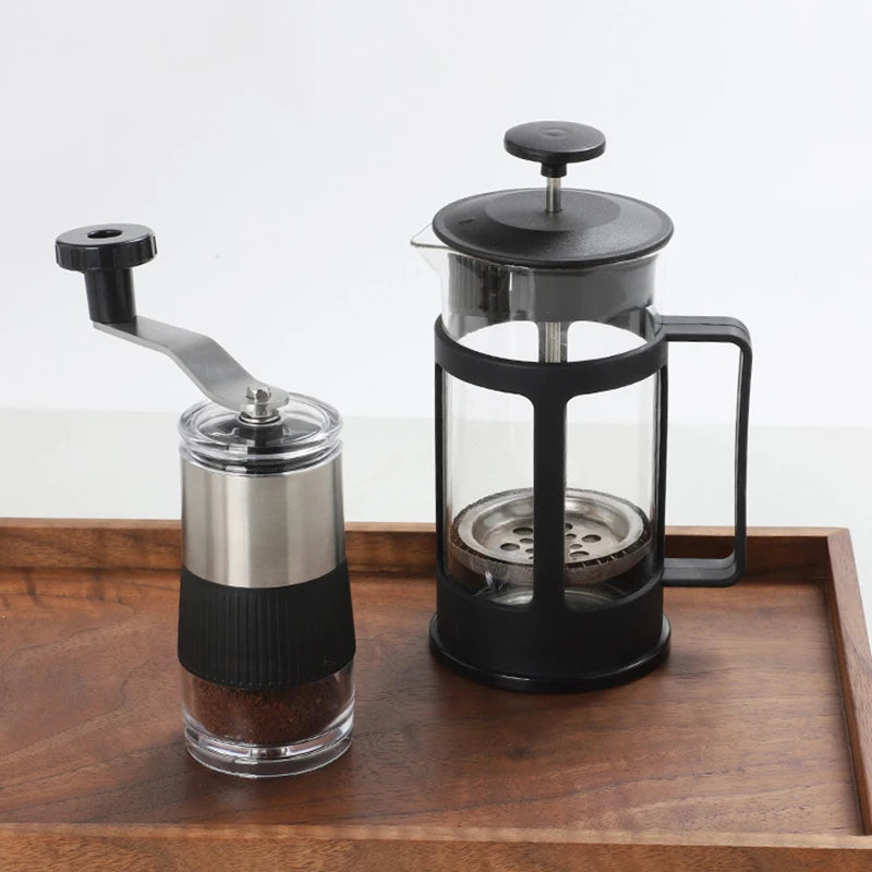 Il macinacaffè su un vassoio di legno accanto a una caffettiera a stantuffo