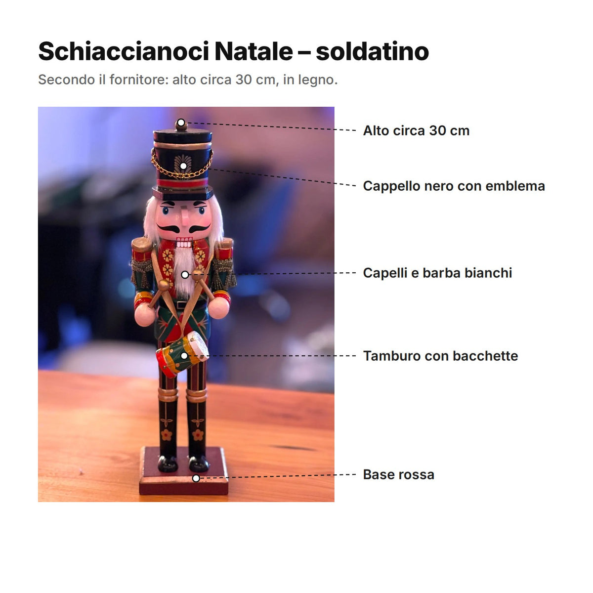Schiaccianoci Natale spiegato: alto circa 30 cm, cappello nero con emblema, capelli e barba bianchi, tamburo con bacchette, base rossa