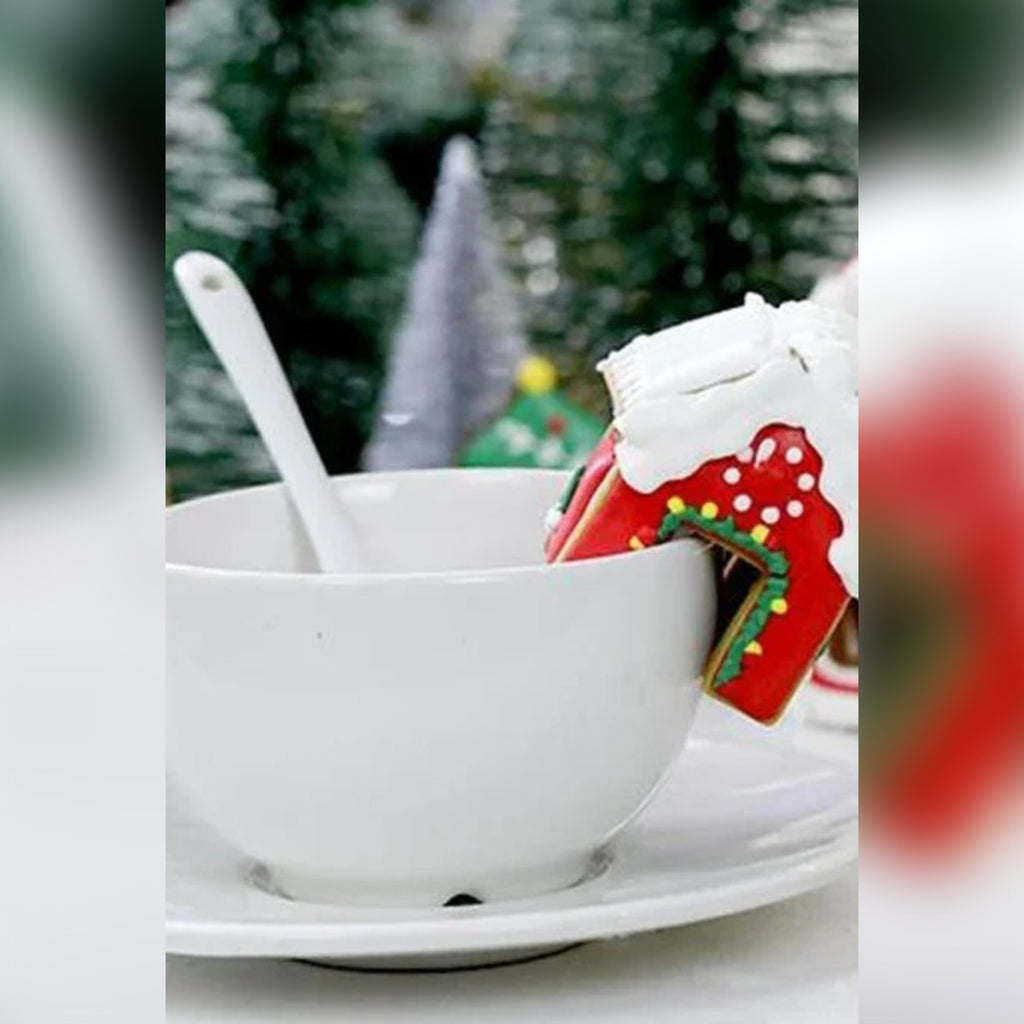 Mini casetta di pan di zenzero decorata, appoggiata sul bordo di una tazza